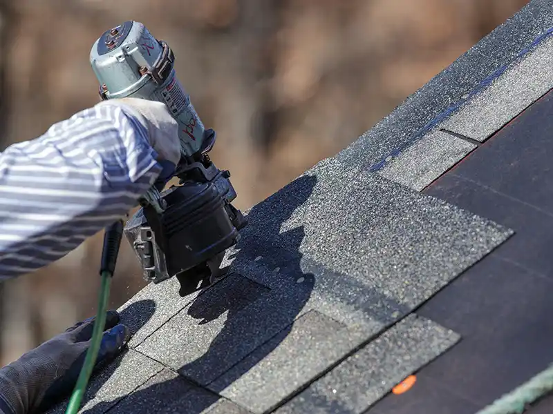 Roofer installing shingles with nailgun